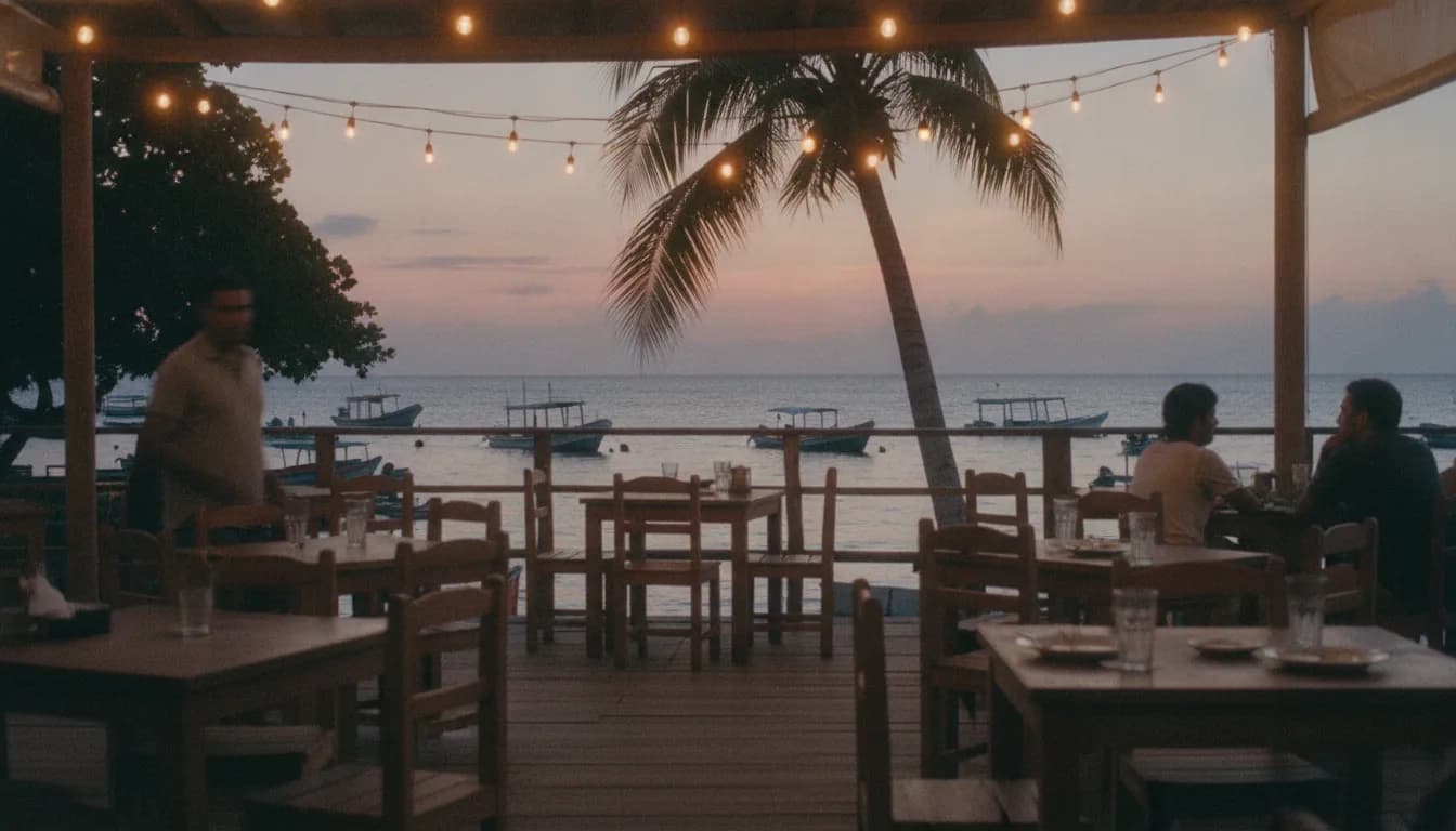 A seafront terrace at sunset, with string lights and boats in the background